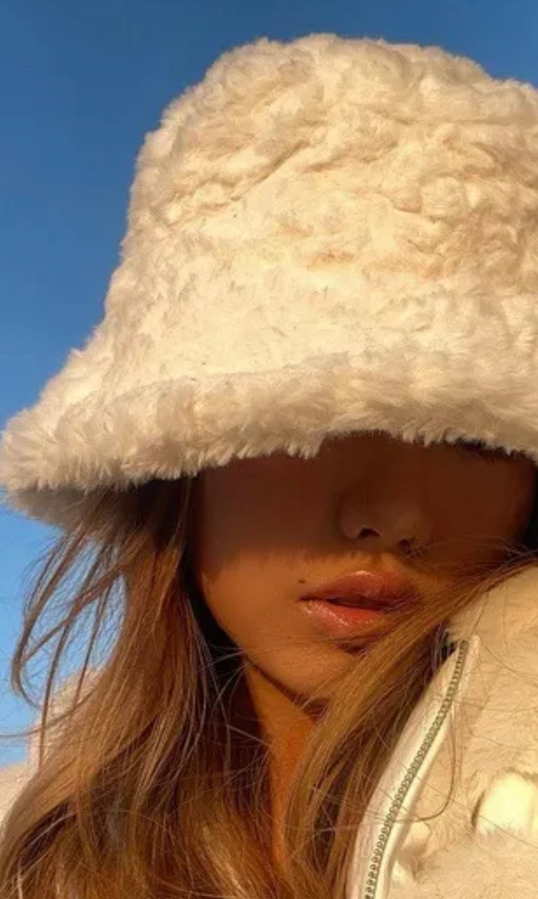 A person wearing a beige faux fur hat with a fluffy brim.
